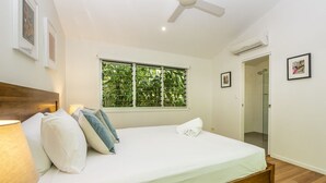 A bedroom with a bed, a ceiling fan, a window with blinds, and a door leading to a bathroom.