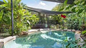 A swimming pool surrounded by tropical plants and a covered seating area.