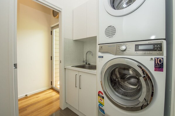 A compact laundry room with a washing machine, a sink, and a small window.