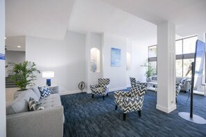 A modern hotel lobby with a grey sofa, patterned armchairs, a potted plant, and a large window. - Indulge at Harbor Towers | Resort-style amenities (Siesta Key)