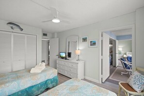 A bedroom with two beds, a dresser, a ceiling fan, and a bathroom visible through an open door. - Indulge at Harbor Towers | Resort-style amenities (Siesta Key)