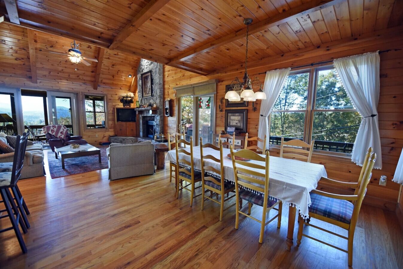 A spacious wooden cabin with a dining area, living room, and large windows offering views of the outdoors.