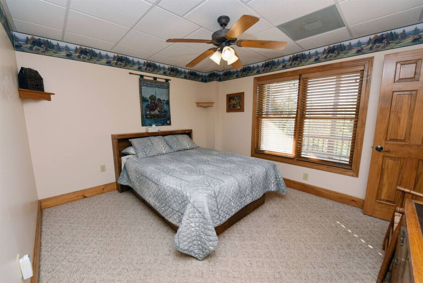 A bedroom with a bed, a ceiling fan, a window with blinds, and a door.