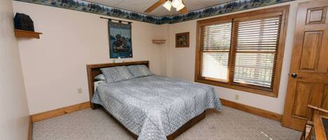 A bedroom with a bed, a ceiling fan, a window with blinds, and a door.