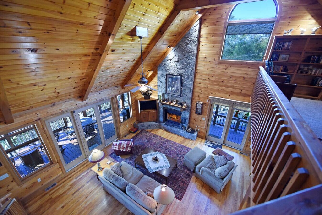 A log cabin with a stone fireplace, wooden floors, and large windows.