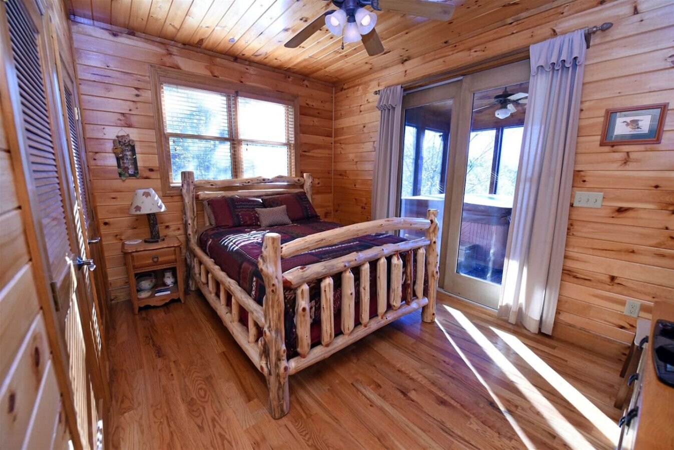 A wooden cabin bedroom with a bed, a nightstand, a lamp, and a ceiling fan.
