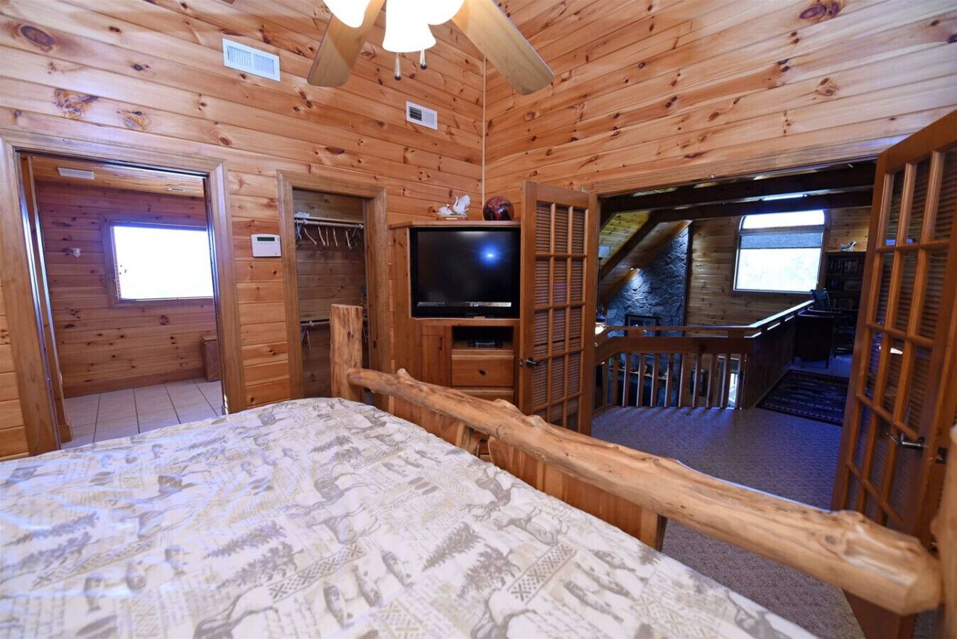 A wooden cabin room with a bed, a television, and a balcony with a stone wall.