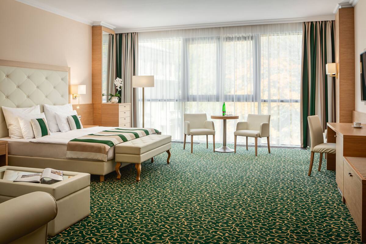 A hotel room with a large bed, a sitting area with chairs, a small table, and a desk.