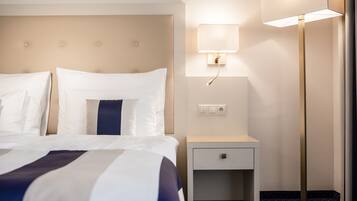 Una habitación de hotel con cama, mesita de noche, lámpara y toma de corriente.