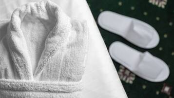 A white bathrobe and white slippers on a bed with a green patterned bedspread.