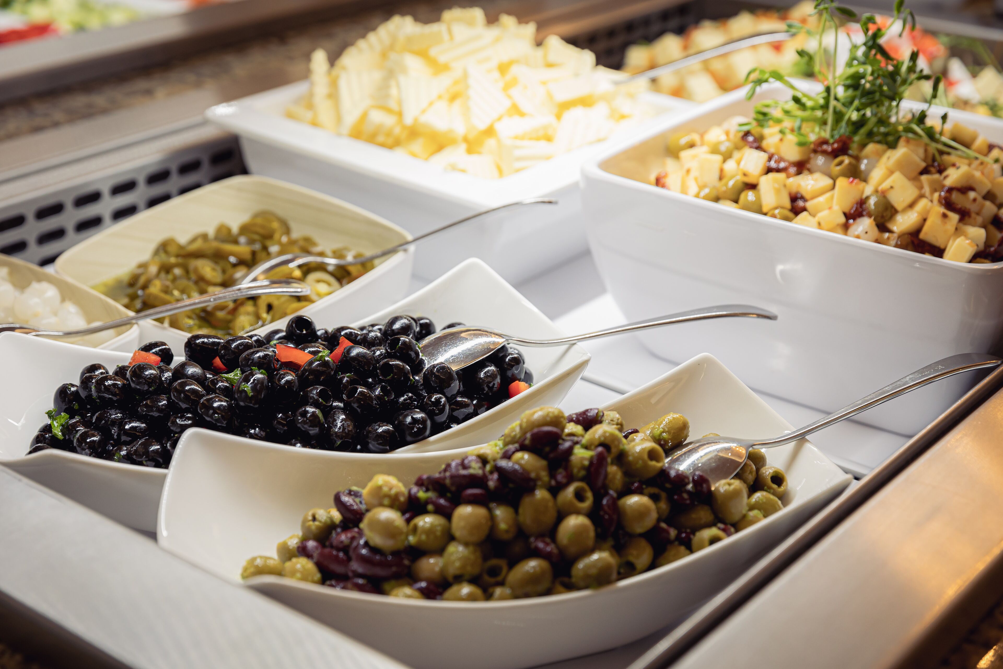 A buffet with various dishes including olives, cheese, and pasta.