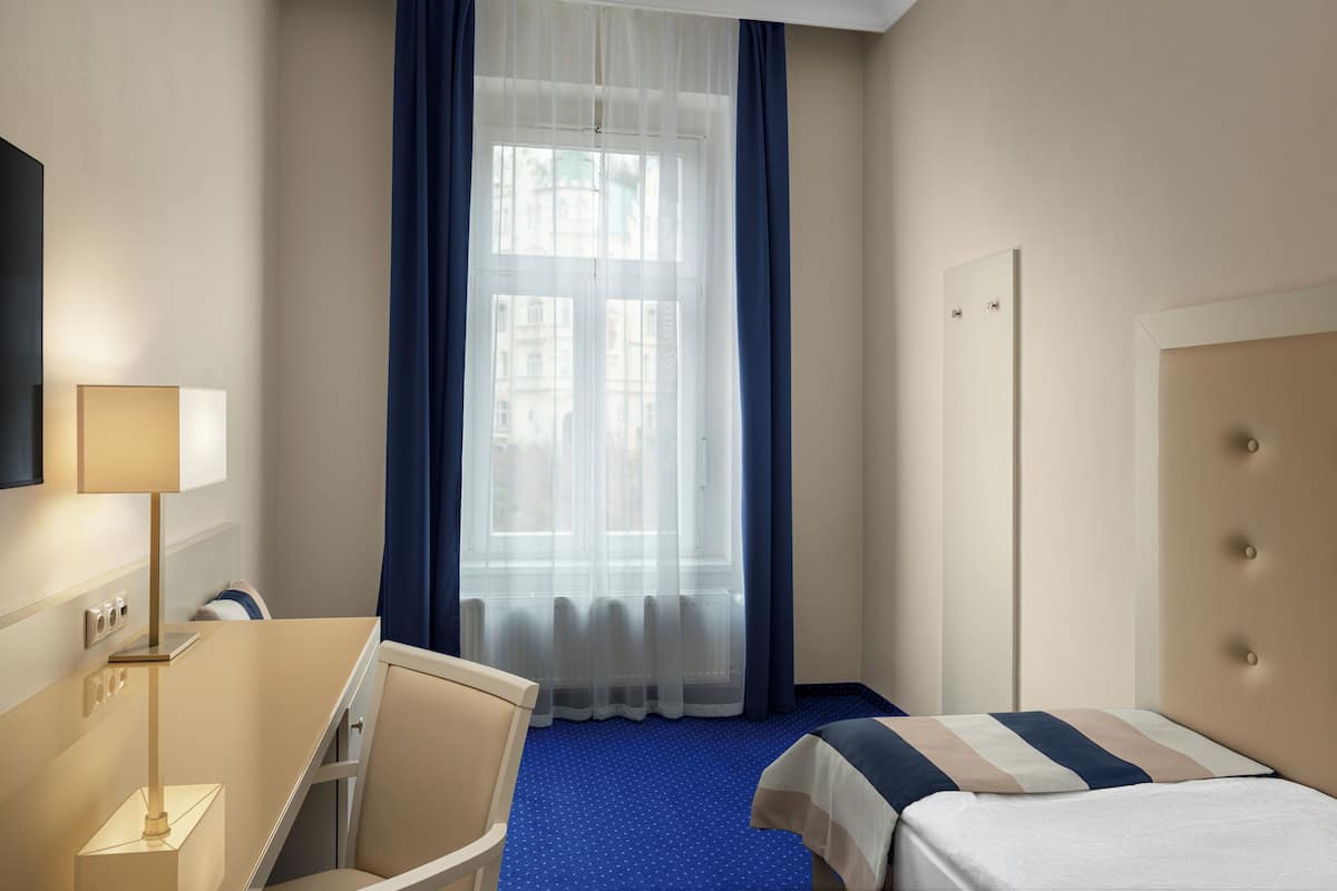 A hotel room with a bed, a desk, a chair, a window with curtains, and a television on the wall.