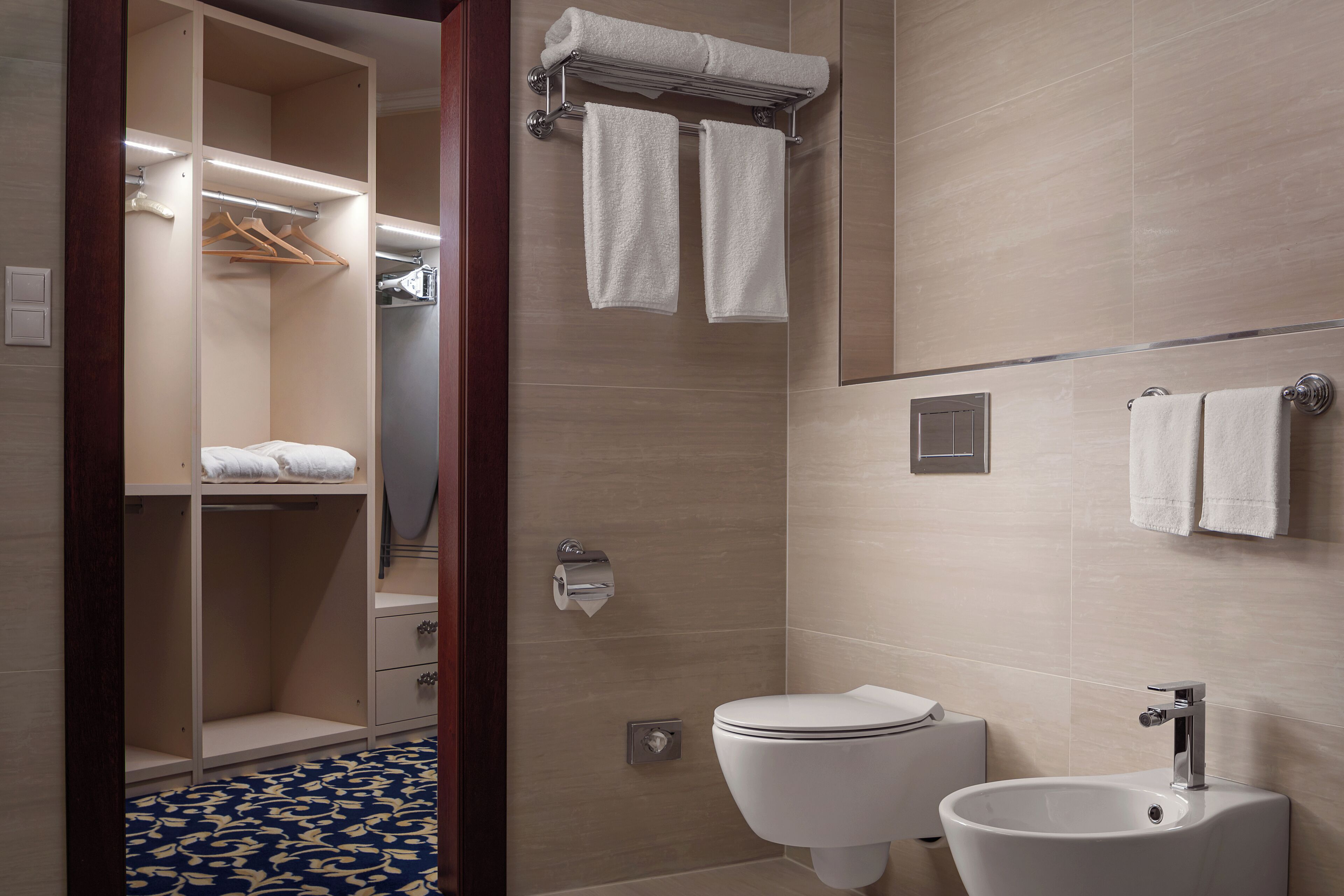 Et moderne badeværelse med toilet, vask, håndklædestang og et walk-in closet med hængende tøj.
