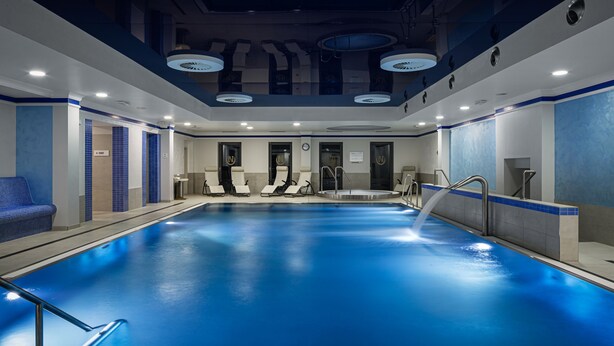 An indoor swimming pool with a blue floor, surrounded by lounge chairs and a seating area. - Hotel Nabokov (Marianske Lazne)