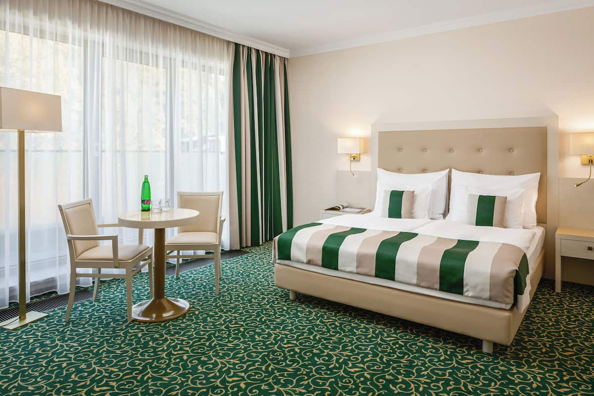 A hotel room with a bed, a chair, a table, and a lamp.