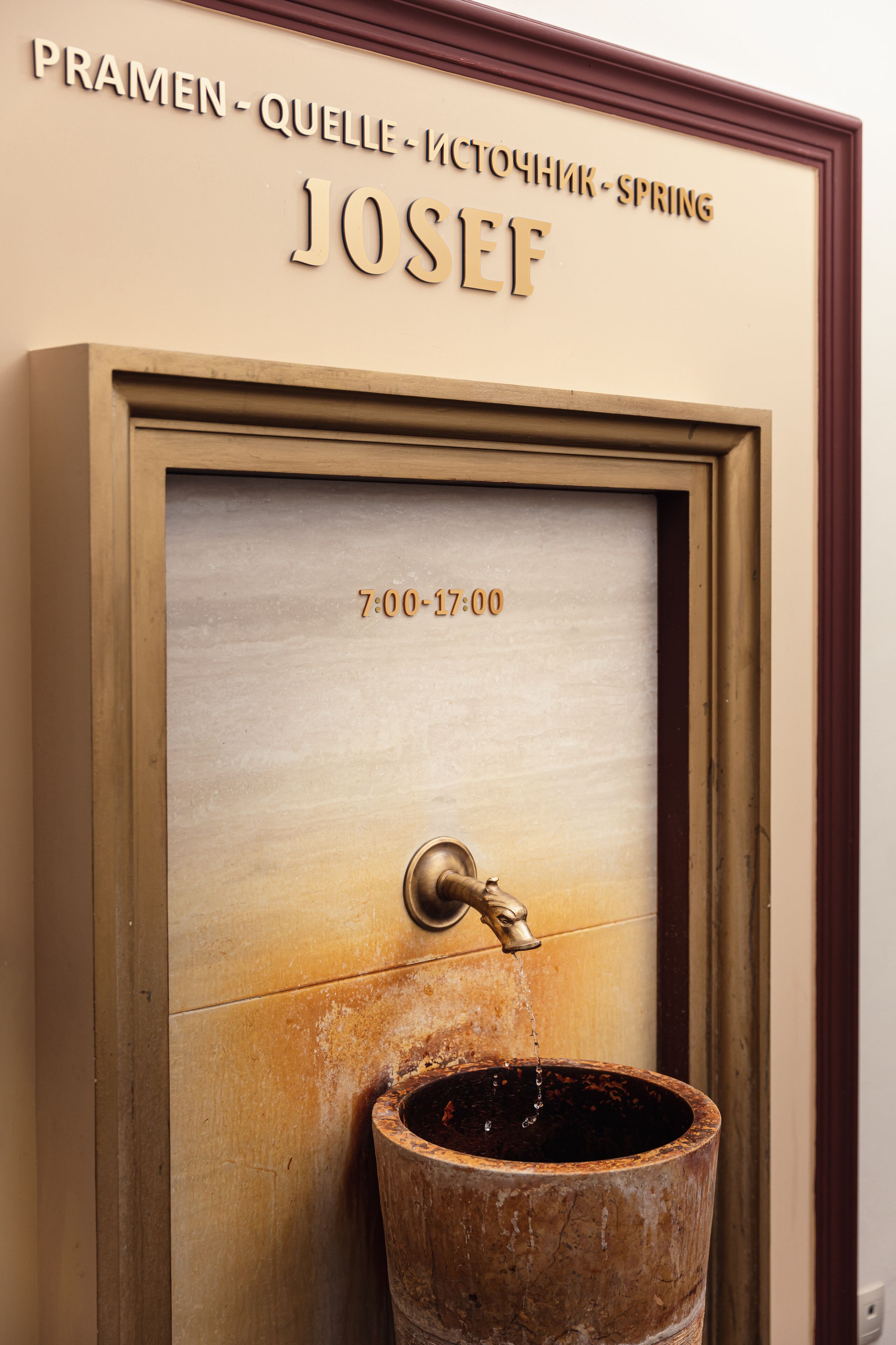 A wooden water fountain with a brass spout and a date sign above it.