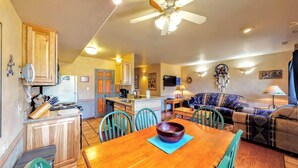 A cozy living area with a dining table, chairs, a sofa, and a kitchen in the background. - Petroglyph Place - 3299, 3 Bedroom Condo (Moab)