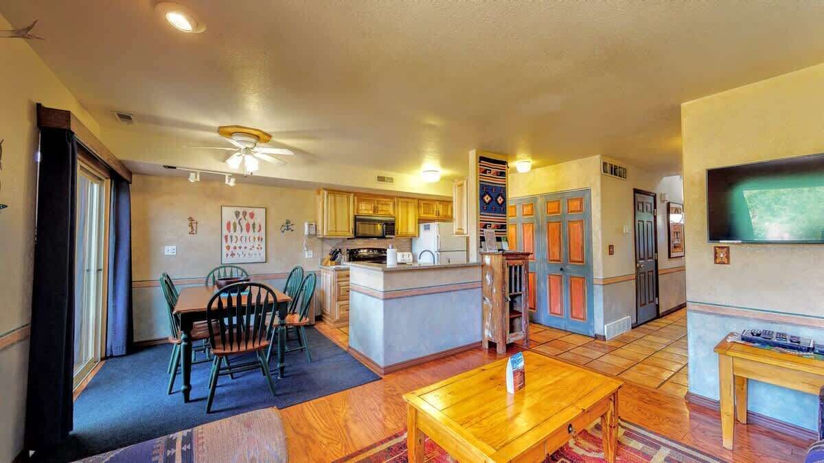 A spacious living area with a dining table, chairs, a kitchen with wooden cabinets, and a ceiling fan.