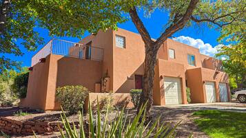 A two-story house with a stucco exterior, a tree in the front yard, and a clear blue sky.