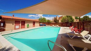 A swimming pool with sun loungers and a shaded area, surrounded by buildings and trees. - Petroglyph Place - 3299, 3 Bedroom Condo (Moab)