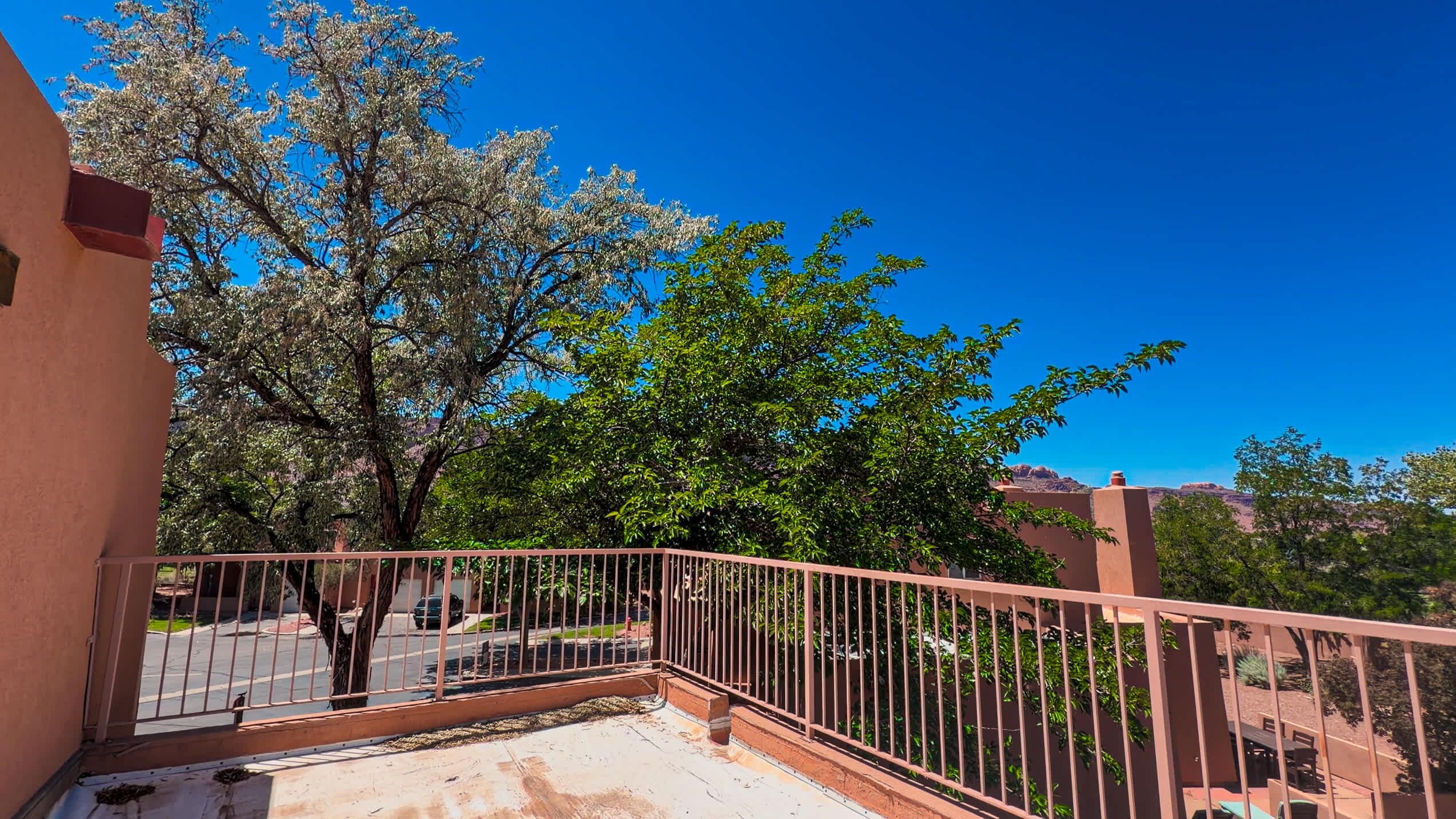 A balcony with a metal railing, a tree with white blossoms, and a clear blue sky.