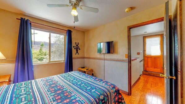 Un dormitorio con cama, ventilador de techo, televisor y puerta que da a otra habitación.