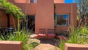 An outdoor patio area with a table and chairs, surrounded by greenery and a building facade. - Petroglyph Place - 3299, 3 Bedroom Condo (Moab)