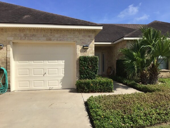 A residential house with a white garage door, a stone facade, and a well-maintained lawn with a palm tree.