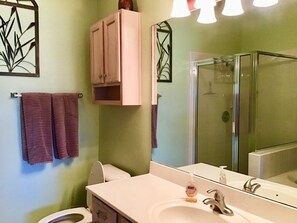 A bathroom with a toilet, sink, and shower. There are towels hanging on the wall and a cabinet above the sink.