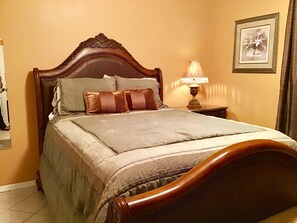 A bedroom with a wooden bed, a bedside table with a lamp, and a framed picture on the wall.