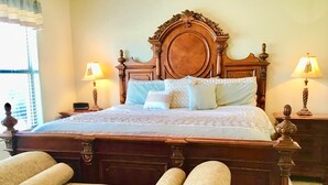 Un lit classique en bois, doté d’une tête de lit travaillée, de deux lampes de chevet et d’une paire de fauteuils rembourrés.