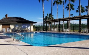 A clear blue pool with a lifeguard stand, lounge chairs, and a covered seating area.