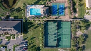 Vue aérienne d’une propriété dotée d’une piscine, de courts de tennis et d’un espace de stationnement.
