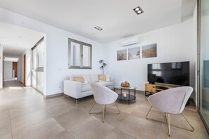 A modern living room with a sofa, two armchairs, a TV, and artwork on the wall.