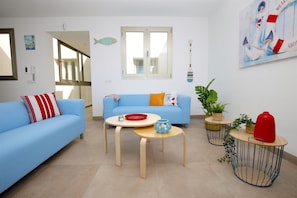 Ein modernes Wohnzimmer mit einem blauen Sofa, zwei runden Holztischen und einem großen Fenster.