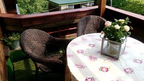 Una terraza de madera con sillas de mimbre y una mesa con mantel floreado.