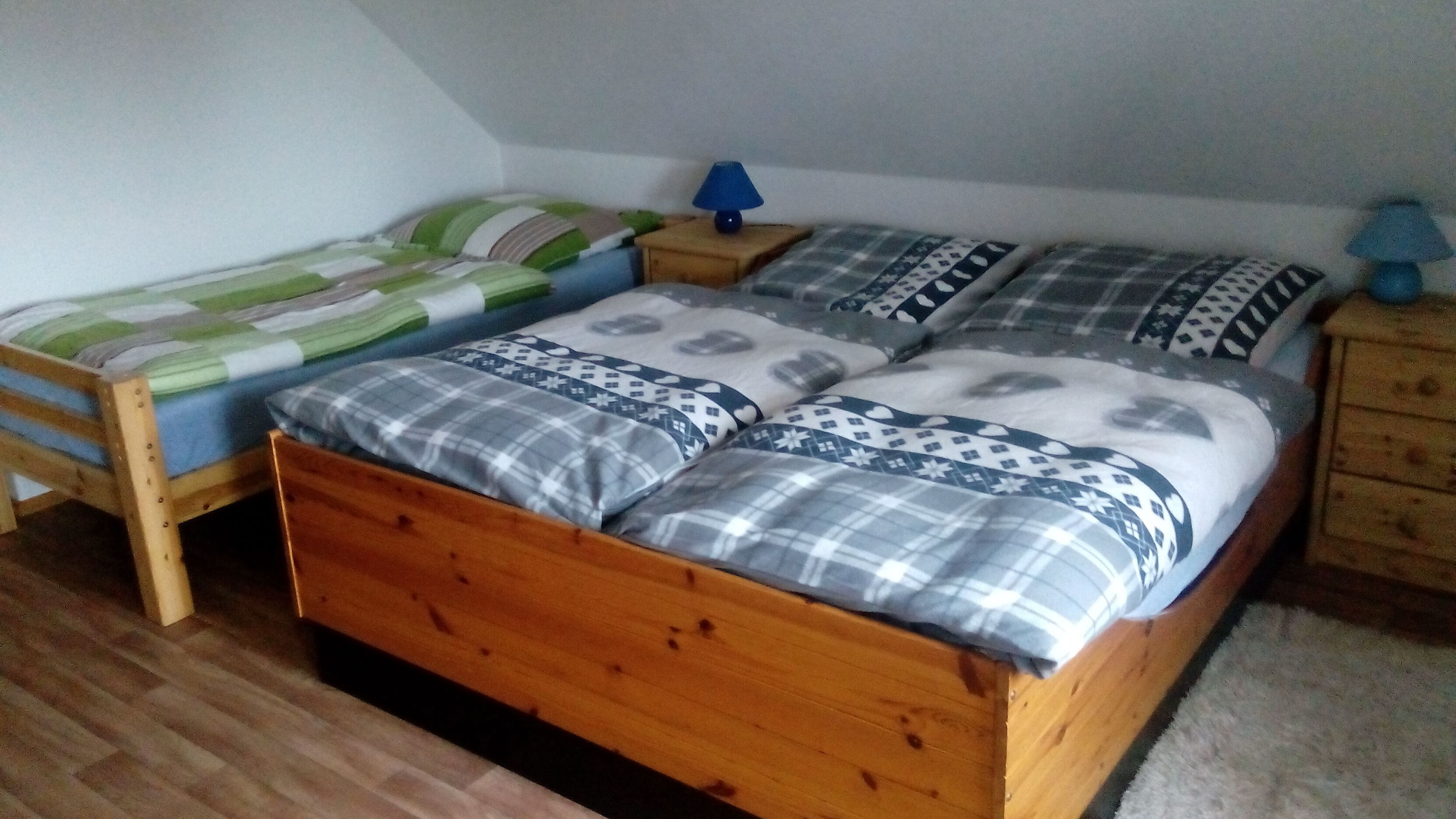 Makuuhuoneessa on puinen sänky, pienempi sänky ja yöpöytä, jossa on lamppu.