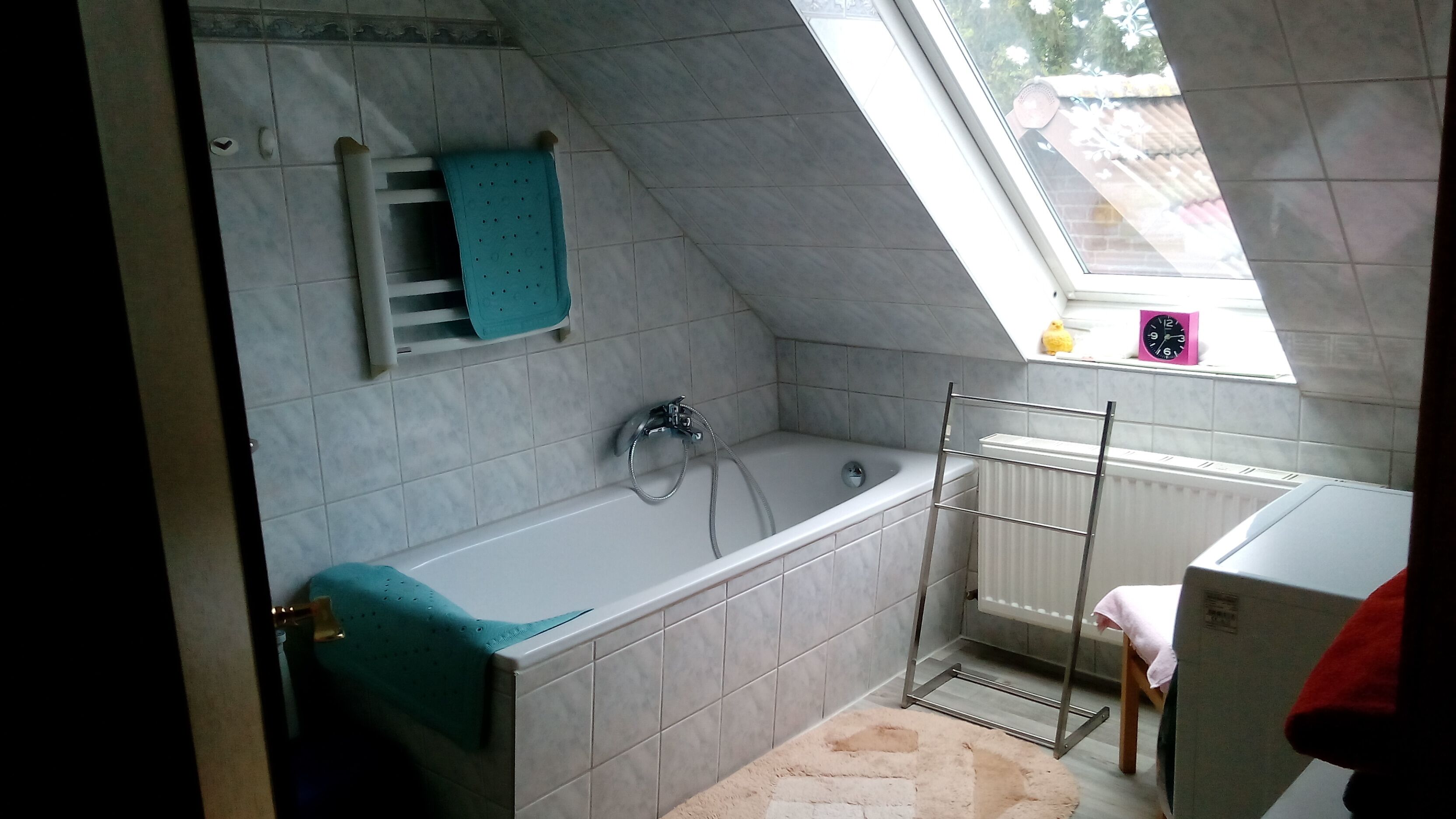 A small, modern bathroom with a sloped ceiling, a bathtub, a shower, and a window providing natural light.