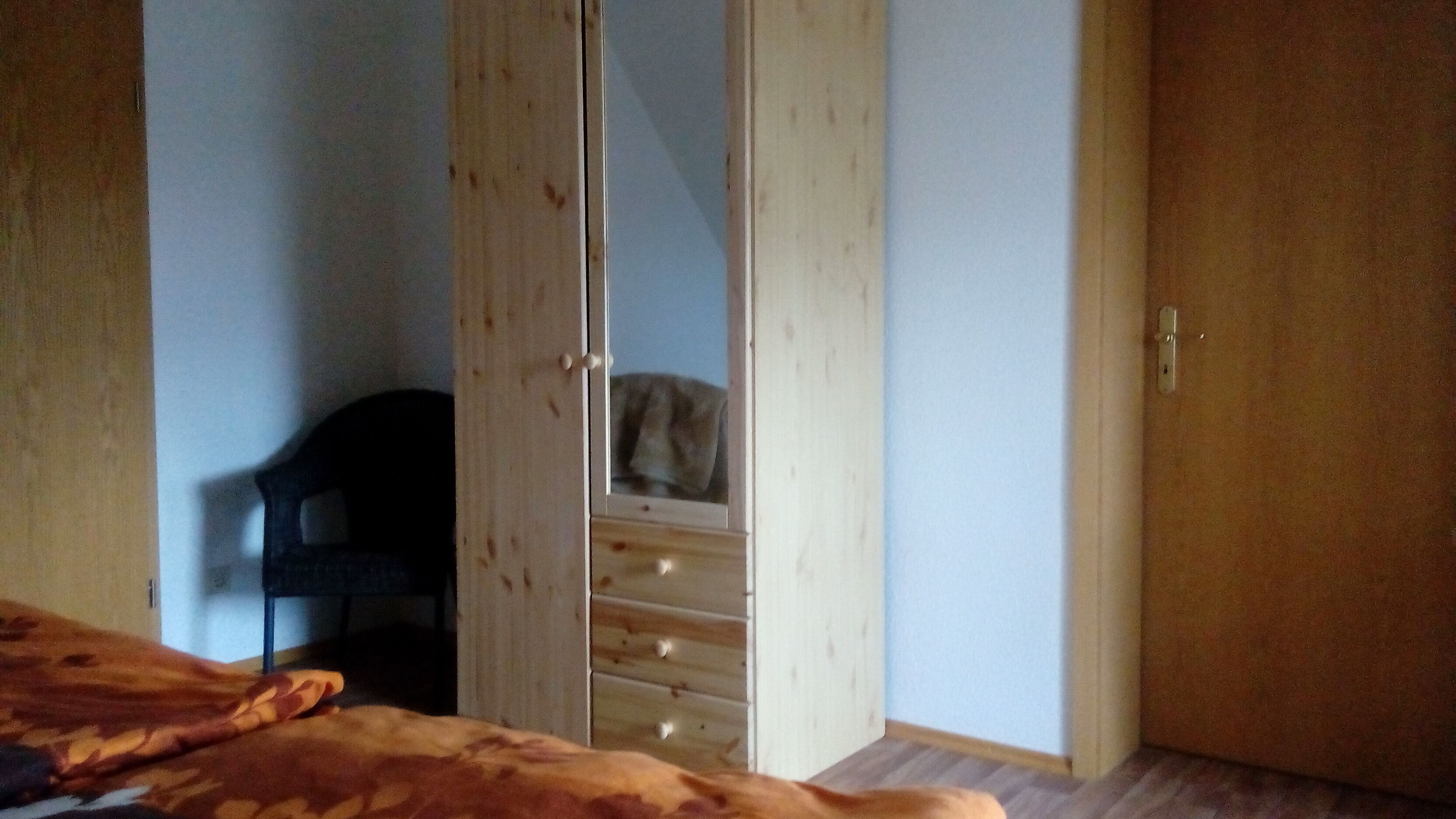 Un dormitorio con cama, armario de madera, silla y cómoda.