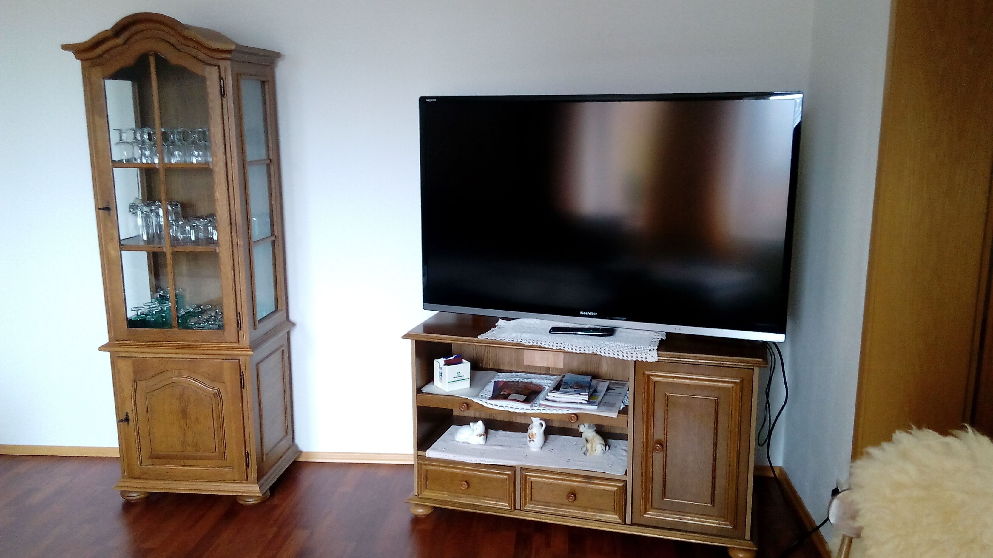 Una sala de estar con un mueble de madera que contiene cristalería y un televisor de pantalla plana sobre un soporte de madera.