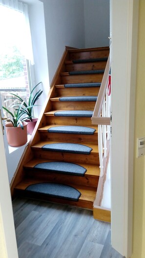 A wooden staircase with blue carpeted steps leading to a landing. - Cozy and generously equipped apartment with balcony in Dörphof (Dörphof)