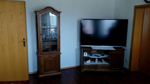 Una habitación con un armario de madera con puertas de cristal, un televisor de pantalla plana sobre un mueble y una puerta de madera.