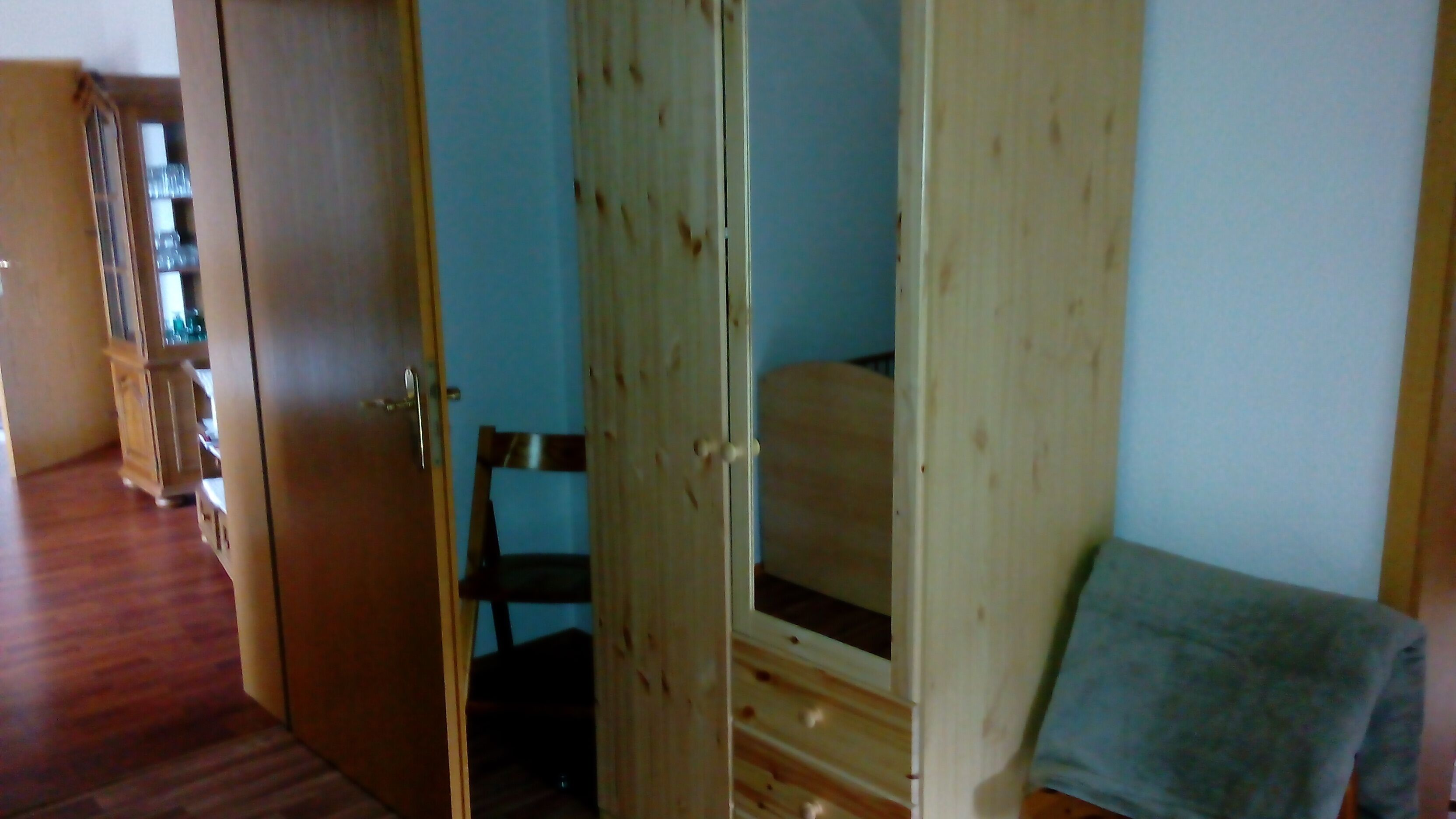 A room with a wooden wardrobe, a chair, and a bed.