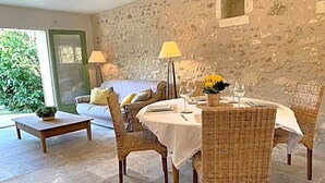 Un coin repas avec des chaises en osier, une table ronde et un mur en pierre.