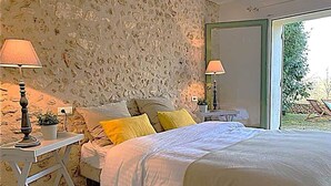 Une chambre avec un mur en pierre, un lit avec une literie blanche, deux lampes de chevet et une vue sur l’extérieur.