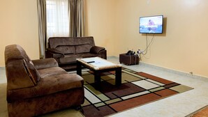 Uma sala de estar com um sofá marrom, uma mesa de centro e uma TV fixada na parede.