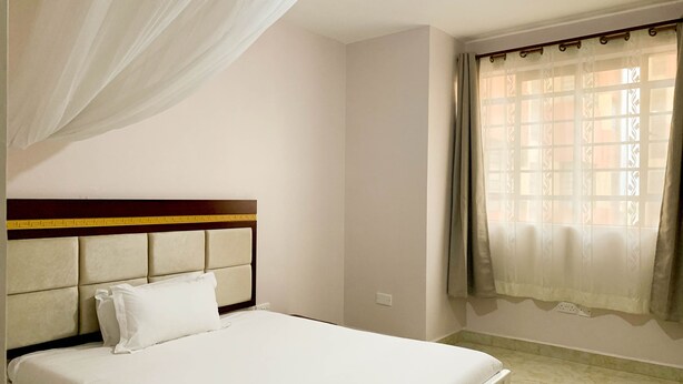 Uma cama bem arrumada com cabeceira, uma janela com cortinas e uma tomada na parede.