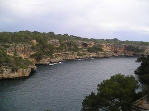 A coastal landscape with rocky cliffs, a body of water, and a historical stone structure. - Hostal Can Jordi (Santanyi)
