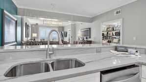 A modern kitchen with a double sink, a dining area with a view, and a living space with a large mirror and artwork. - Inn at Crystal Beach 305 * Gulf Front with Beach Chair Set. Onsite dining! (Destin)