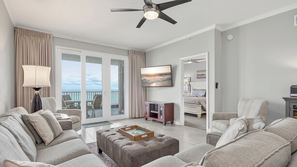 A spacious living room with a large sofa set, a ceiling fan, and a television on the wall. - Inn at Crystal Beach 305 * Gulf Front with Beach Chair Set. Onsite dining! (Destin)